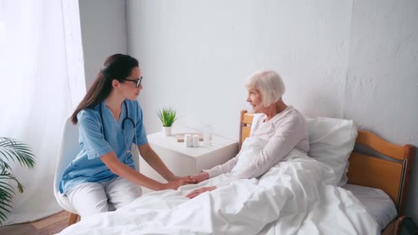 Oudere Vrouw Zitten Bed Praten Met Brunette Geriatrische Verpleegster — Stockvideo