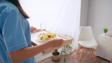 Genç hemşire yaşlı hastaya kahvaltı tepsisi taşıyor. 