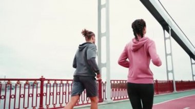 Arkaplanda bulutlu gökyüzü olan köprü yolu boyunca koşan çiftin arka planı