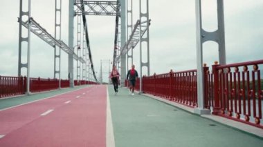 Arka planda bulutlu gökyüzü ve ağır çekim ile köprüde koşan iki koşucu