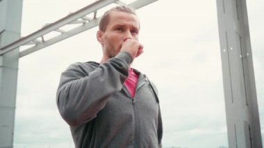 Köprüde nefes darlığı çeken koşucu duruyor. Arka planda bulutlu bir gökyüzü var.