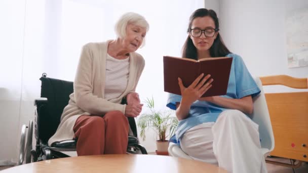 Starší Žena Mluví Zatímco Mladá Zdravotní Sestra Čtení Knihy — Stock video