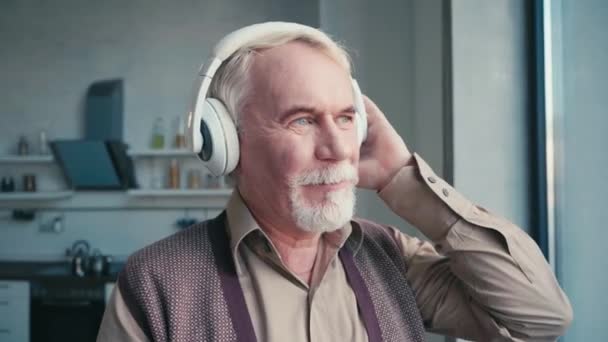Älterer Mann Mit Kopfhörern Hört Musik Während Hause Fenster Steht — Stockvideo