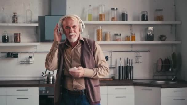 Kulaklıklı Dans Eden Mutfakta Baş Parmağını Gösteren Mutlu Yaşlı Adam — Stok video