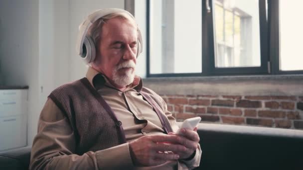 Grauhaariger Mann Mit Kopfhörer Und Smartphone Der Hause Musik Hört — Stockvideo