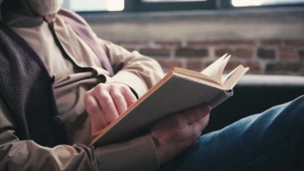 Senior Άνθρωπος Κάθεται Στον Καναπέ Και Φύλλα Μέσα Από Βιβλίο — Αρχείο Βίντεο