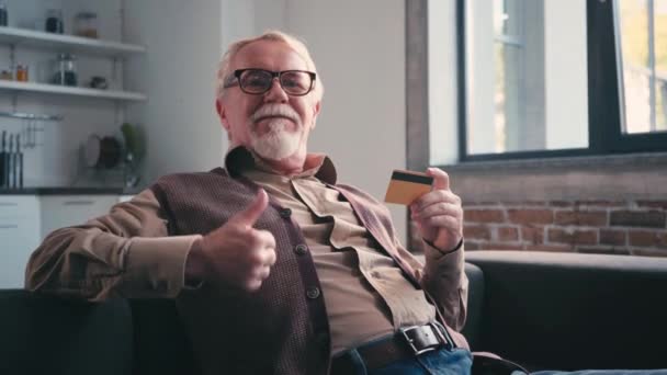 Lachende Senior Man Toont Duim Omhoog Houdt Credit Card Thuis — Stockvideo