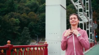 Köprüde koşan ve arka planda doğa olan gülümseyen sporcu kadın.