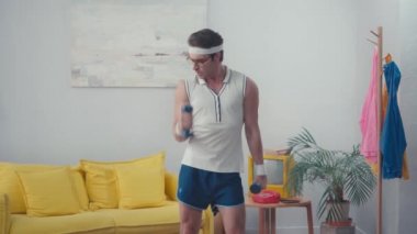 Oturma odasında ağırlık kaldıran komik sporcunun ön görüntüsü, retro spor kavramı