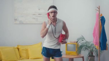 Enerjik sporcu, evde kalçalarını sallarken ev telefonuyla konuşuyor. 