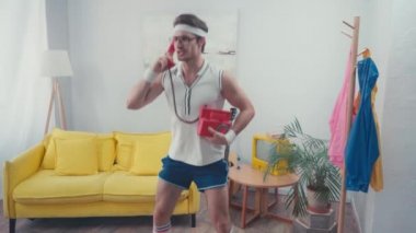 Sporcu oturma odasında ev telefonuyla konuşurken çömeliyor.