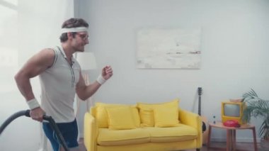 Enerji dolu sporcu oturma odasında elektrikli süpürgeyle ritmik dans ediyor.