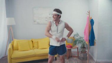 Eli kalçasında, oturma odasında dans eden enerjik sporcunun ön görüntüsü.