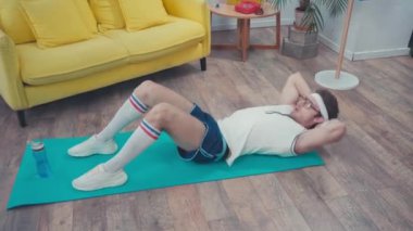 Sporcu oturma odasındaki spor minderinin yanında karın kası yapıyor.