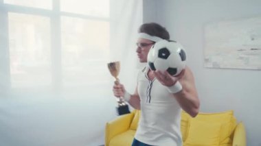 Kupalı ve futbol toplu heyecanlı futbolcu, evde zaferi kutluyor.
