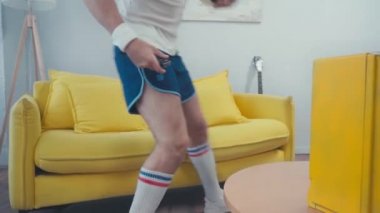 Futbol topuyla kanepede oturan ve televizyonu açan futbolcu. 