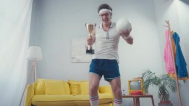 Oturma odasında spor topu ve kupayla dans eden enerjik sporcu.