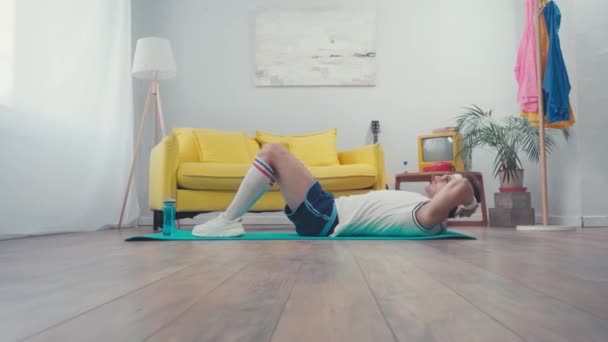 リビングルームのフィットネスマットに座っているスポーツマンの表面レベル — ストック動画