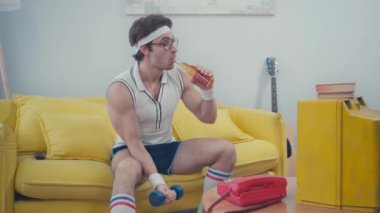Sporcu kanepede otururken içki içiyor ve dambılı kaldırıyor.