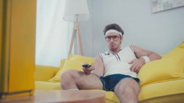 Sporcu, kanalı değiştirirken karnını kaşıyarak burnunu karıştırıyor.