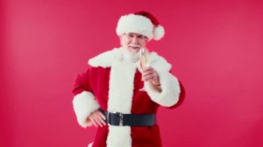 Neşeli Noel Baba, elleri kalçasında kırmızı bardakta şampanya tutuyor.