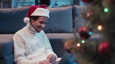 Noel Baba şapkalı mutlu Afro-Amerikan adam video çağrısını yaparken el sallıyor.