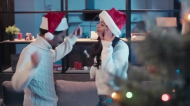 Kırmızı Noel Baba şapkalı neşeli Afro-Amerikan çift evde dans ediyor.