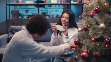 Erkek arkadaşının köknar dekorasyonu yaparken fotoğrafını çeken Afrikalı Amerikalı bir kadının ilgi odağı.