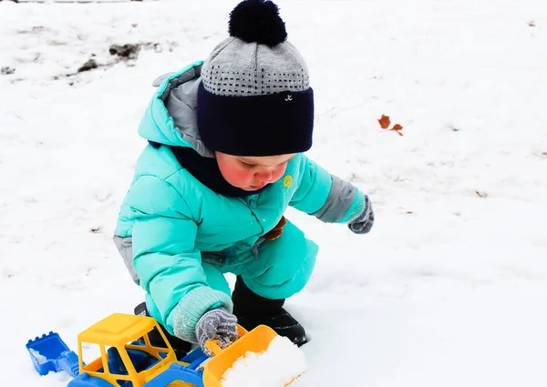 ショベルと庭遊びでの少年 庭には雪します 少年は冬の服に身を包んだ アクアのパッド入りのダウンのコート ニット帽子 ミトン ショベル イエロー ブルー ストック画像