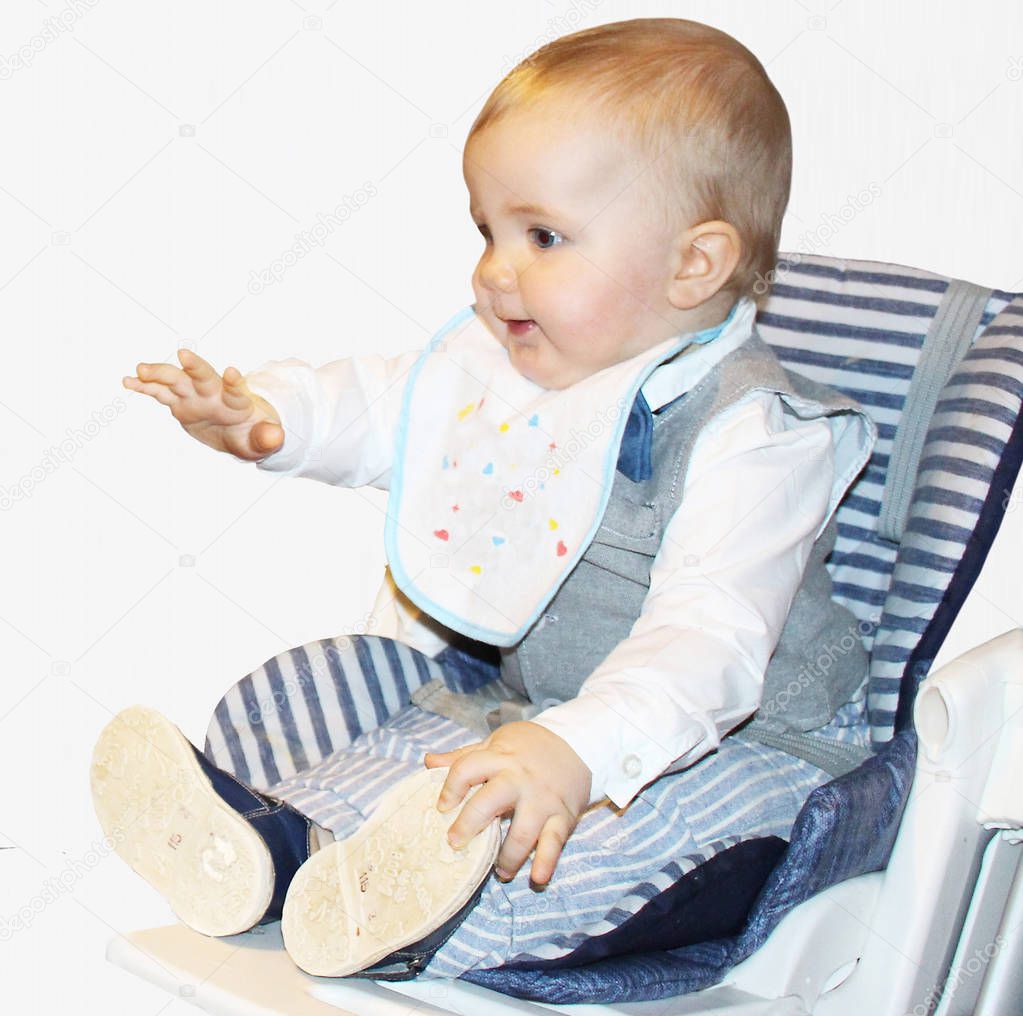 The child is already a year old. Baby is sitting in a child seat. He is wearing a smart suit: a gray vest, a white shirt and striped pants. Baby eats.