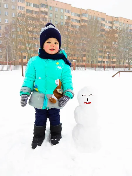 赤ちゃんと雪だるま ミンスク市 2018 の男の子は 雪だるまを作られます その少年は冬服 緑のダウン ジャケット マフラー ミトン ロイヤリティフリーのストック写真