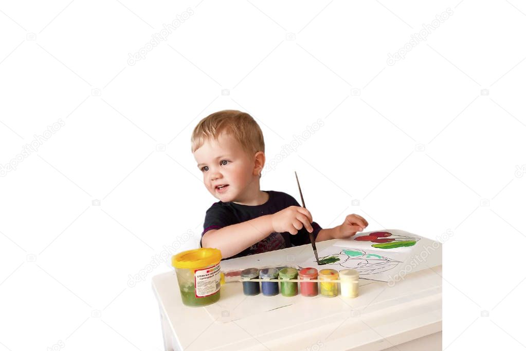  The child draws. City apartment. 08/02/2019. The boy sits at the training table. On the table you want paint with a coloring book.Boy holding a brush in his hand. He smiles. He is wearing a navy t-shirt. 