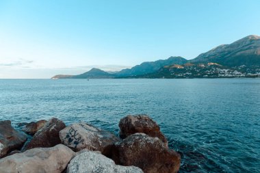 Sahilde büyük taşlar. Şehir, deniz feneri, gemiler arka planı. Sabah erken