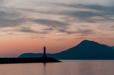 Deniz feneri günbatımı. Dağlar fonunda.