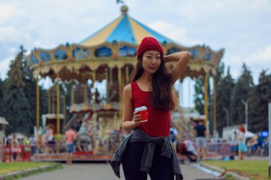 kız bir salıncak önünde duruyor ve kahve içiyor