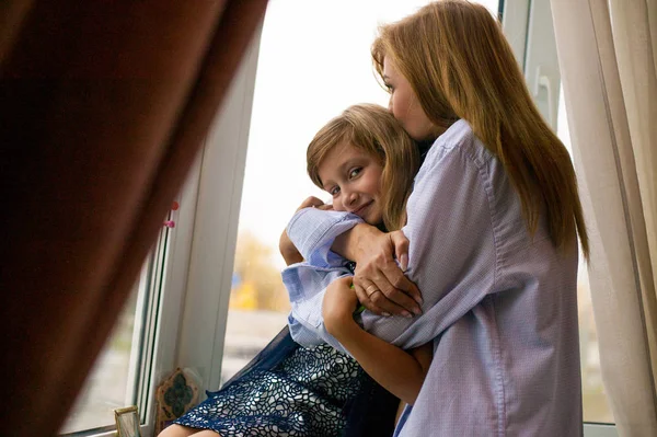 happy family near the window. mother and child hugging near the window of the house. Mom and daughter love each other.