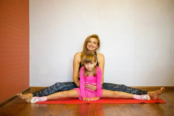 Mom and daughter on yoga mat smiling. Health family do pilates. Family doing sports, doing exercises at home.