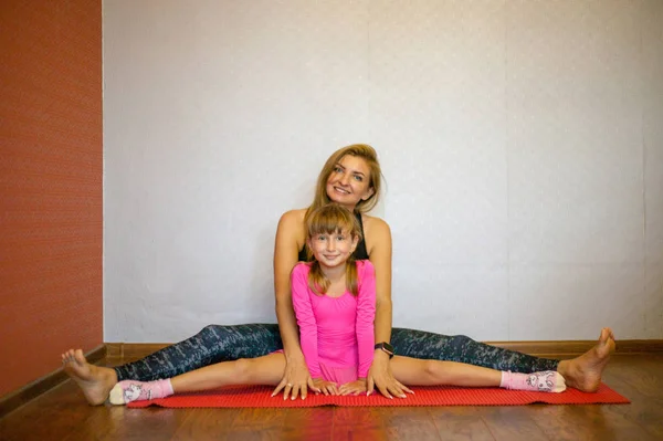Mom and daughter on yoga mat smiling. Health family do pilates. Family doing sports, Mom and daughter are sitting on the splits.