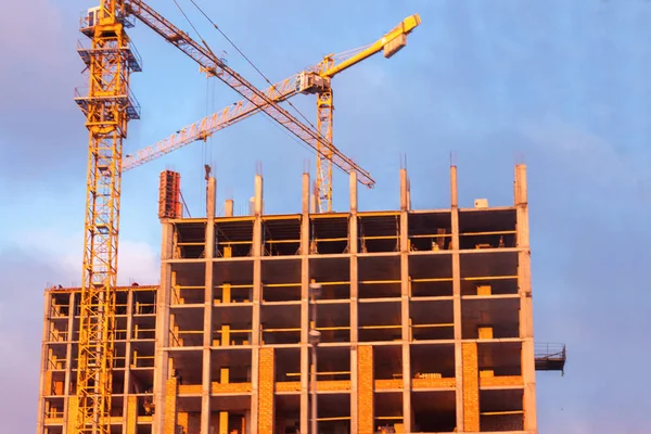 New buildings and cranes for construction in the background of blue sky at sunset.