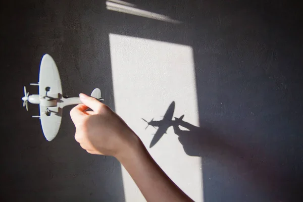 Interesting abstract background with a shadow on the concrete wall from the blinds. A hand is holding a plane and there is a shadow on the wall.