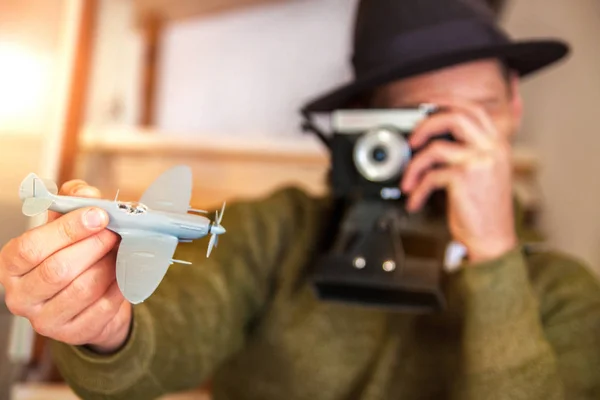 一个戴着帽子的快乐青年拿着一架飞机 地图正在公寓里准备旅行 他的脖子上挂着一台相机 — 图库照片