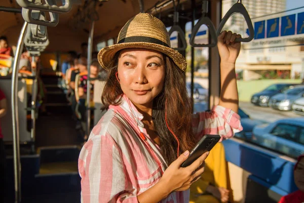 Asian girl with earphone standing on the bus enjoying the trip.