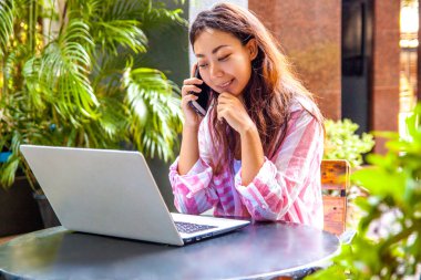 Kafede dizüstü bilgisayar ve akıllı telefon kullanan mutlu kadın görüntüsü. Bir kafede otururken ve bilgisayarda çalışan genç güzel kız.