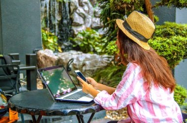 Kafede dizüstü bilgisayar ve akıllı telefon kullanan mutlu kadın görüntüsü. Bir kafede otururken ve bilgisayarda çalışan genç güzel kız.