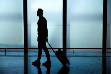 İş adamı havaalanı koridorunda bavulunu taşıyarak çıkış kapılarına doğru yürüyor..