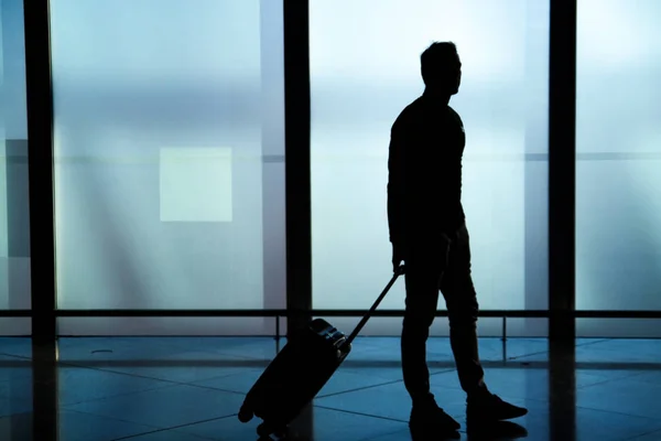 Businessman dragging a small carry on luggage suitcase at airport corridor walking to departure gates.