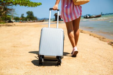 Tropikal bir plajda bir bavul ile güzel genç kadın. Arka planda mavi deniz. Seyahat konsepti.