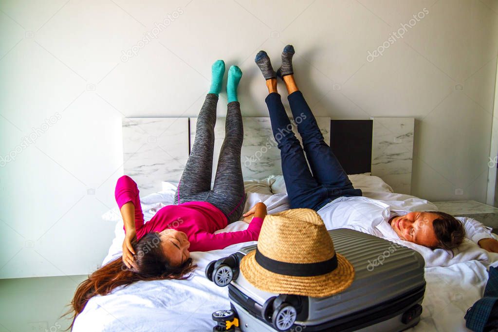 Couple lies on the bed with suitcase. Fees on journey concept. Luggage preparation.