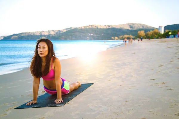 young fitness asian woman on the beach doing core exercises as part of her healthy crossfit training rutine. fit female model in sports clothing.