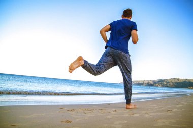 Genç adam plajda spor kıyafetleriyle koşuyor.. 